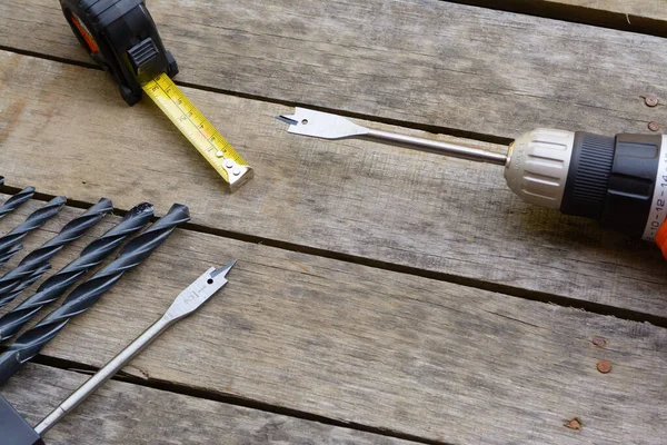 Power drill tape measure with many drill bits on an old wood deck.