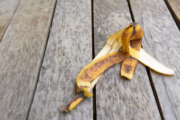 褐色和黄色折皱的香蕉皮躺在带有黑斑的旧灰色木头表面上 — 图库照片