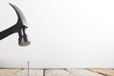 Siyah bir çekiç metal bir çiviyi tahtaya çakıyor.