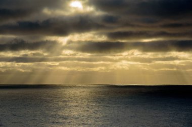 Parlak güneş ışınları dalgalanan denizin yüzeyinde yoğun kara bulutlar arasında parlıyor.