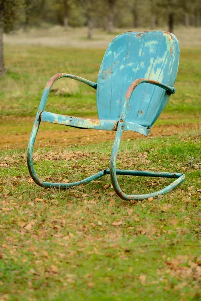 Old rough rusty blue chair placed on green meadow