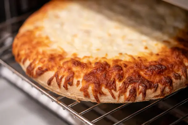 Taze pişmiş bir pizza, bir ekmek kızartma makinesinin içindeki tel askıda oturur, peyniri köpüklü ve altın rengi kahverengidir, tadını çıkarmaya hazırdır..