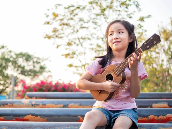 stock image Little asian child girl play the ukulele, in the garden on the Steel pipe