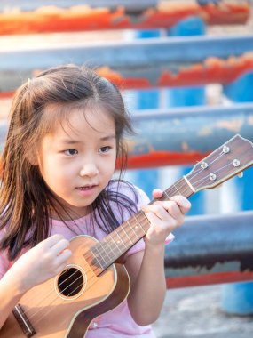 Küçük Asyalı kız ukulele çalıyor, bahçede çelik boruyla, pratik yapıyor