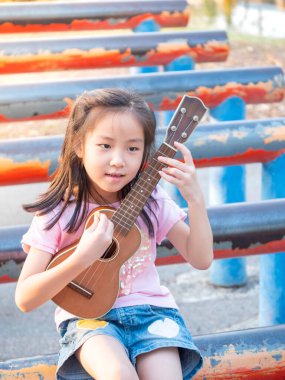 Küçük Asyalı kız ukulele çalıyor, bahçede çelik boruyla, pratik yapıyor