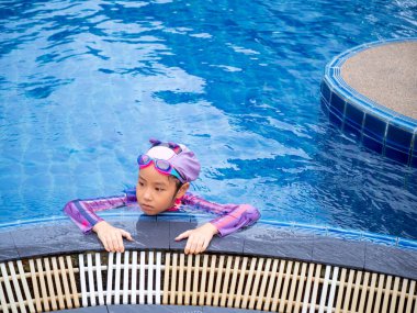 Yüzme havuzu öğrenmek için mayo giyen Asyalı çocuk ya da çocuk tekmeleme tahtasında yüzmeyi öğrenir ve antrenman yapar.