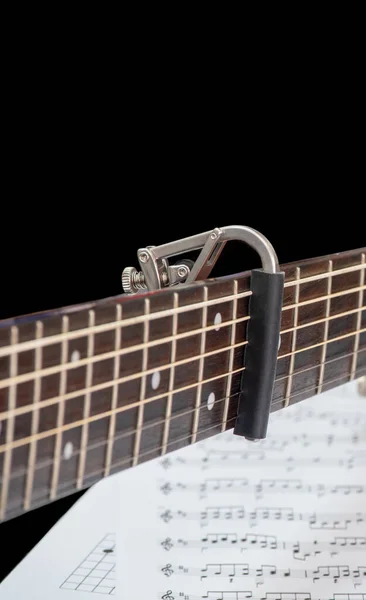 卡波在声学吉他手脖子上 得分笔记在卡波和吉他手下面 铝制卡波 卡波选择性聚焦 — 图库照片