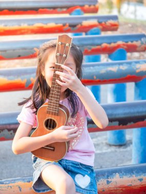 Küçük Asyalı kız ukulele çalıyor, bahçede çelik boruyla, pratik yapıyor