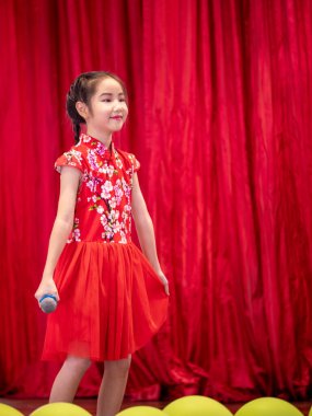 Asyalı kız okul etkinliği gününde sahnede şarkı söylüyor, Qipao tarzı giyiniyor, kırmızı perde arkası.