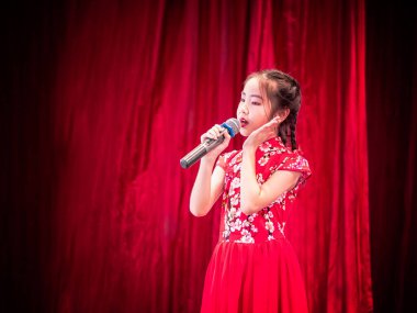 Asyalı kız okul etkinliği gününde sahnede şarkı söylüyor, Qipao tarzı giyiniyor, kırmızı perde arkası.