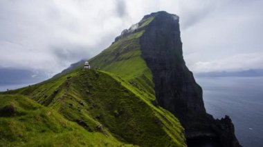 Kallur deniz fenerinin Danimarka 'nın Faroe Adaları' ndaki yeşil tepelerde zaman aşımına uğraması.