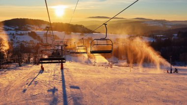 Ski lift empty ropeway on hilghland alpine mountain winter resort on bright sunny evening . Ski chairlift cable way with people enjoy skiing and snowboarding. Sunset sky backlit shining on background clipart