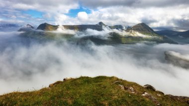 Okyanusla kaplı dağ manzarası. Faroe Adaları 'ndaki Eysturoy Adası' ndaki Funningur fiyordunun üzerinde sis var..