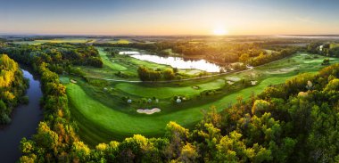 Golf sahası manzarası, yeşil çim yolları ve ormanla dramatik gündoğumunda.