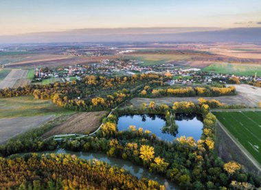 Gün batımında kırsal alanda göl, drone manzarası. Göllü kırsal alan. Tarlaları olan bir gölet. Ülkedeki yeşil tarlalar ve tarım arazileri. Göldeki köy.