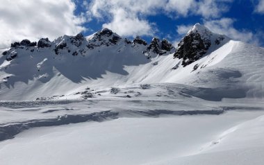 Karlı bir dağ yamacında duran kayakçı. Resmedilmeye değer karla kaplı. Arkaplanda bulutlu mavi bir gökyüzünün altında zirveler. Avusturya Obertauern