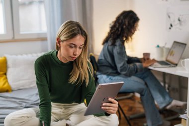 Üniversite öğrencisi odada dijital tablet kullanıyor.