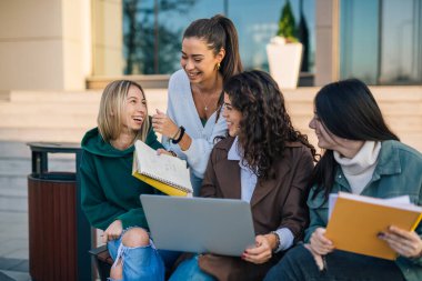 Üniversite kampüsündeki beyaz kız öğrenciler dizüstü bilgisayar kullanıyorlar.