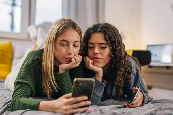 stock image female friends lay on bed in room and using mobile phone