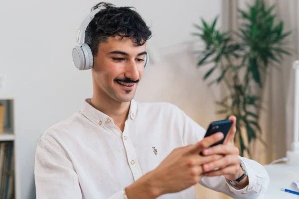 stock image european young adult man with mustaches with headphones using mobile phone