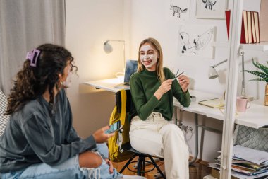 İki ergen arkadaş yüz maskeleriyle sohbet ediyorlar.