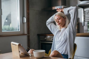 Kadın esniyor ve mutfakta kahvaltı yapıyor.