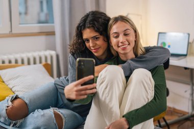 İki arkadaş telefona bakarken sarılıyor.