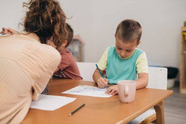 Anaokulunda resim çizen genç çocuk.