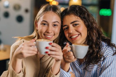 İki genç kadın oturup kahve içiyorlar.