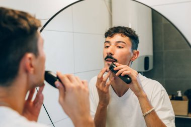 Adam aynanın önünde sakalını kesiyor.