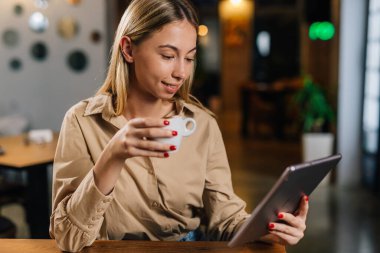 Genç bir kadın kahve içiyor ve tablete bakıyor.