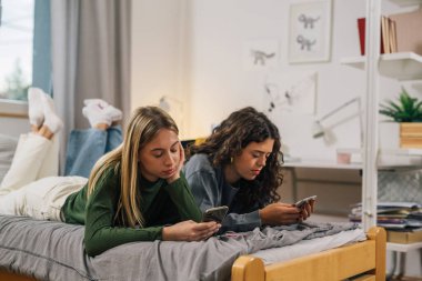 İki yakın arkadaş yatağa uzanıp telefonlarına bakıyorlar.