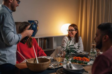 Ev sahibi arkadaşları için bir şişe şarap açar.