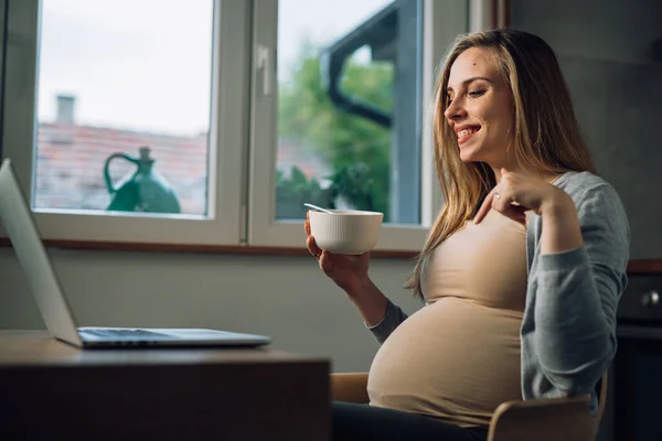 Pregnant woman points to her belly on a video call