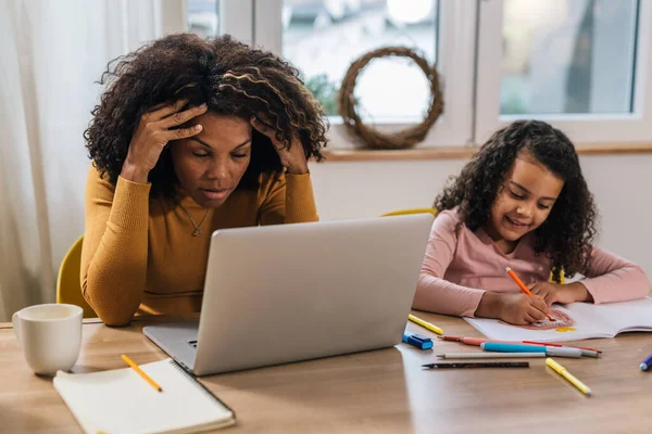 Stressed mother remote working at home next to her daughter