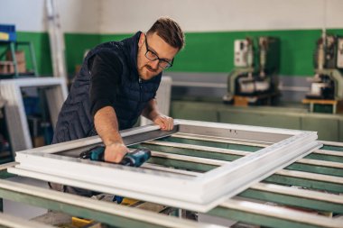 Atölyede PVC pencere çerçevesini vidalayan işçi