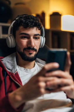 Adam evde kulaklıkla telefon kullanıyor.