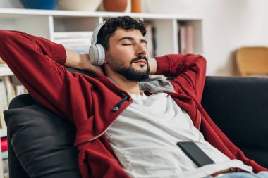 Bir adam evde dinlenirken kulaklıkla müzik dinler.