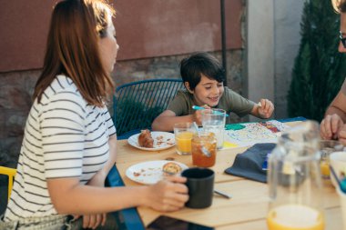 Küçük çocuk kahvaltı saatinde arka bahçedeki masaya resim çizer.