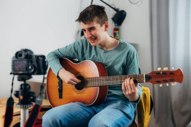 The teenage boy smile at the camera while playing the guitar