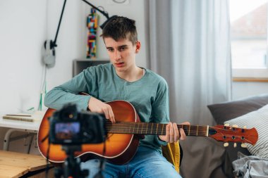 Young adolescent boy is recording himself playing an acoustic guitar