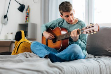 Young teenage boy practices guitar