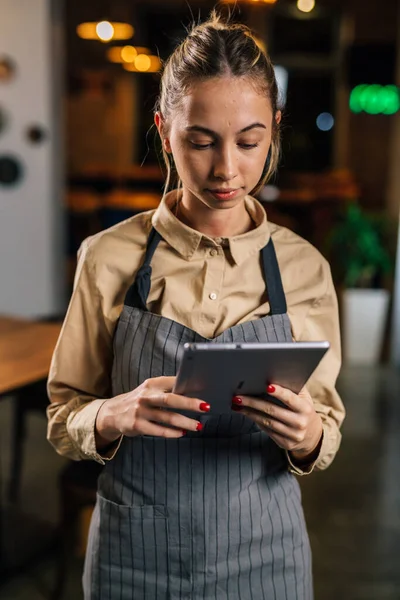 A blonde waitress works in a restaurant and checks orders on tablet