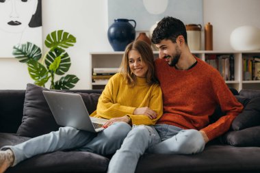 Genç çift kanepede oturur ve dizüstü bilgisayara bakar.