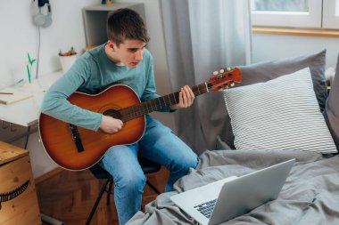Teenage boy practices the guitar at home