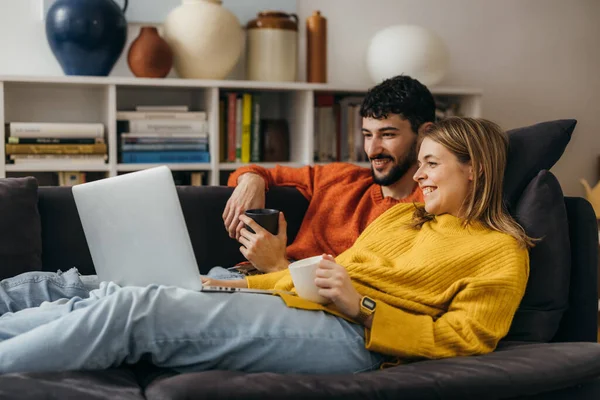 Kanepede film izleyen genç bir çiftin yan görüntüsü.