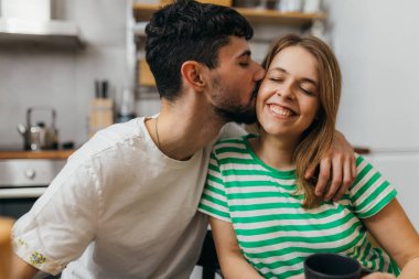 man kissing his girlfriend having breakfast in kitchen