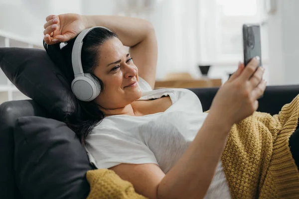 Caucasian woman is relaxing on the sofa and listening to enjoyable music