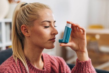 Close up view of a blonde woman inhaling medicine threw asthma pump clipart