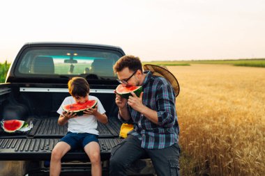 Father and son are enjoying a sweet watermelon o a hot day